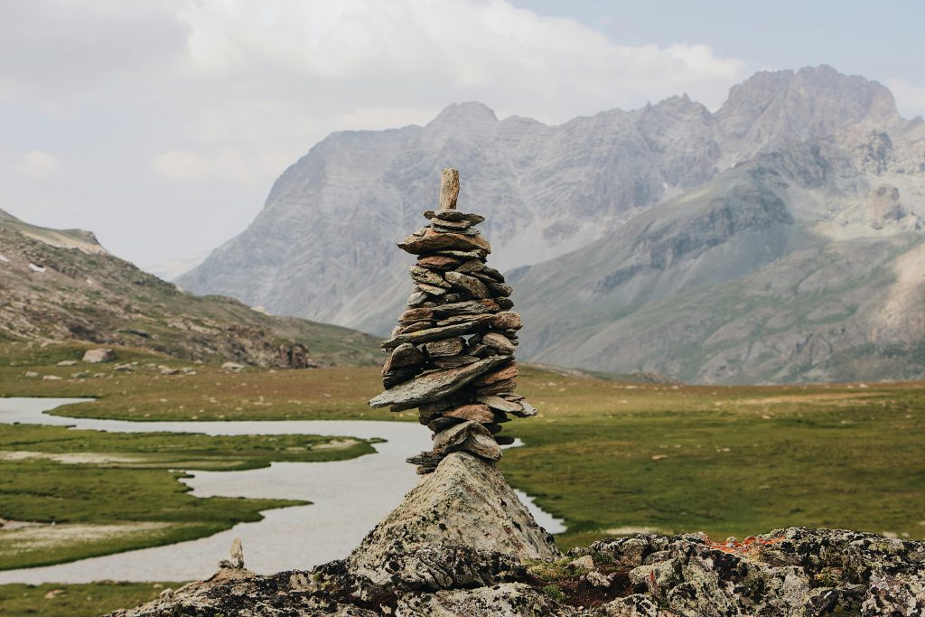A serene scene of a stone cairn in front of majestic mountains and winding stream.