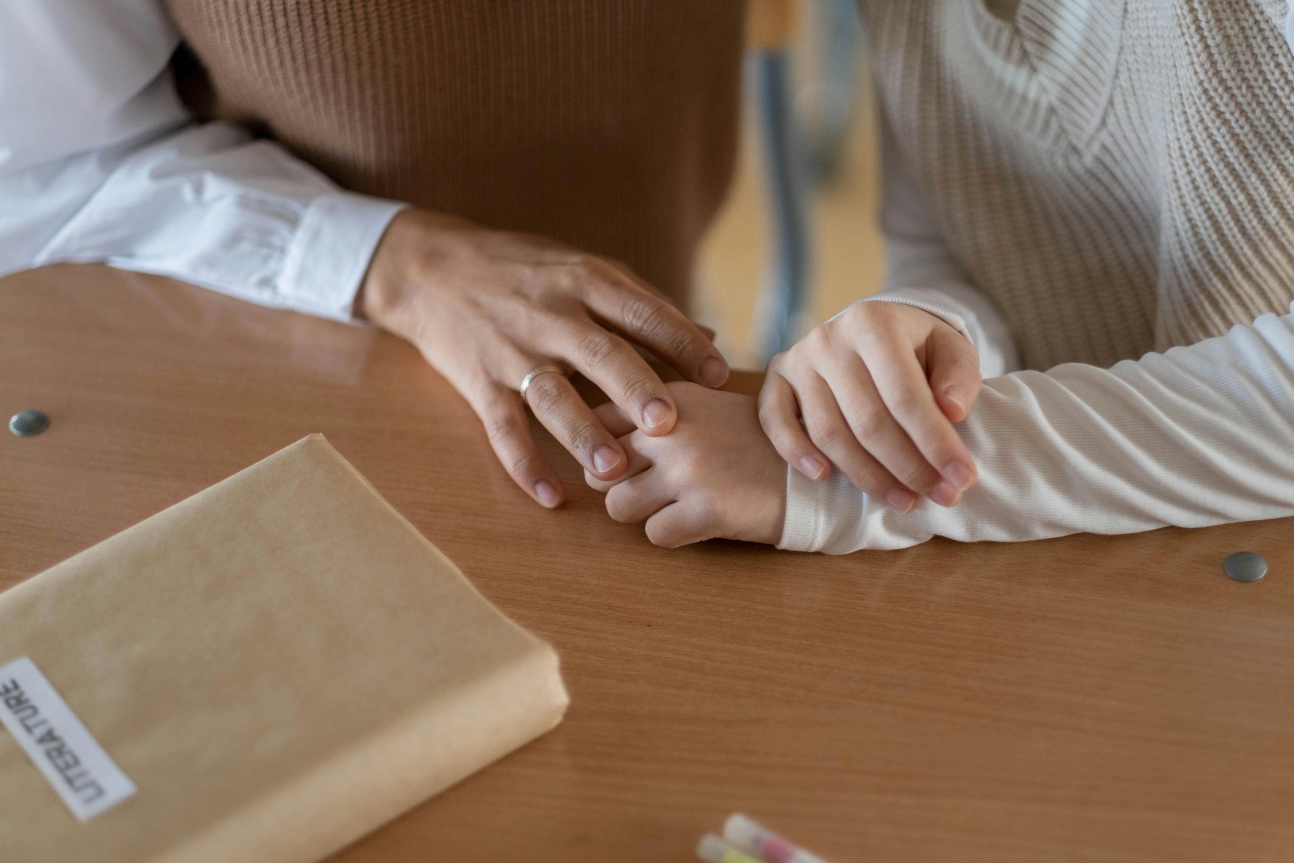 A warm moment captured as comforting hands rest on a table with a book nearby.